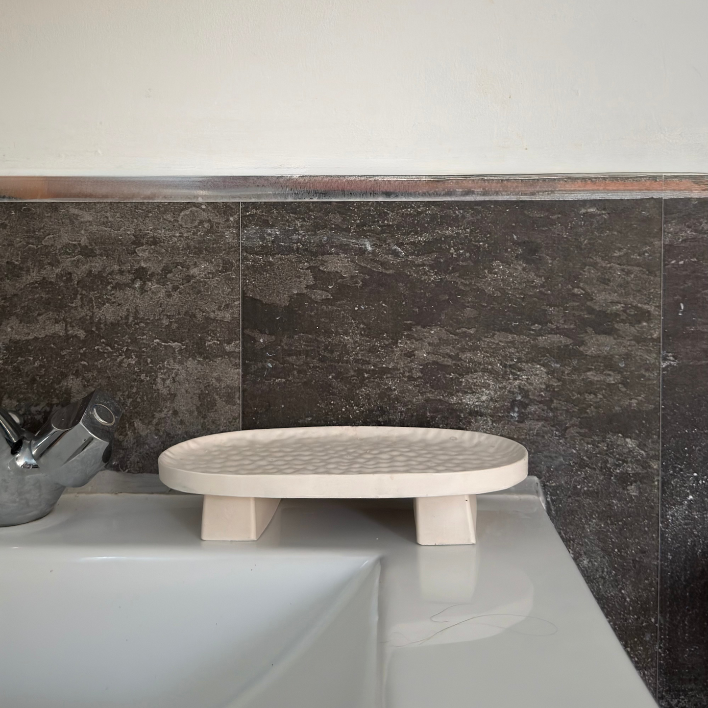 Malmo Home Poise Oval plinth empty on a bathroom surface next to a sink with dark marble tiles behind